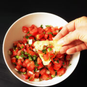 dipping chip in white bowl of pico de gallo.