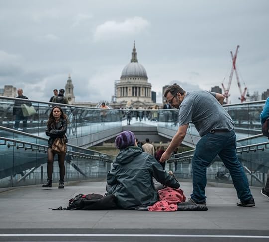 A homeless woman sits on the ground and a man hands her money. St Pauls Cathedral is in the background.
