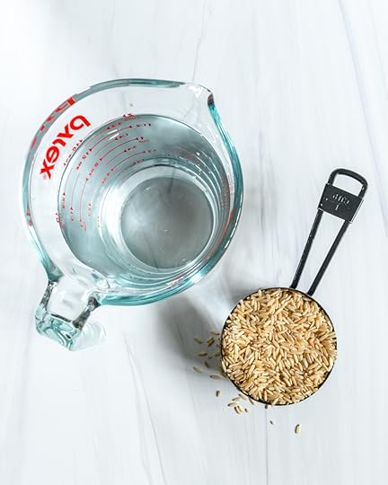 Liquid Measuring Cup with Water and a Cup Measurement With UnCooked Brown Rice On a Marble White Surface