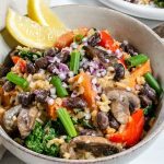 Bowl of veggie filled rice pilaf with two wedges of lemon in the side