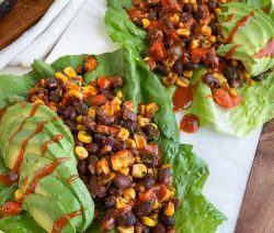 Two lettuce wraps filled with a mix of beans and corn and topped with sliced avocado and hot sauce