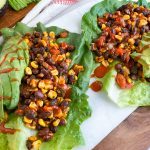 Two lettuce wraps filled with a mix of beans and corn and topped with sliced avocado and hot sauce