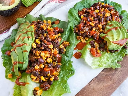 Two lettuce wraps filled with a mix of beans and corn and topped with sliced avocado and hot sauce