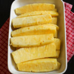 spears of cut pineapple lined up in ceramic dish.