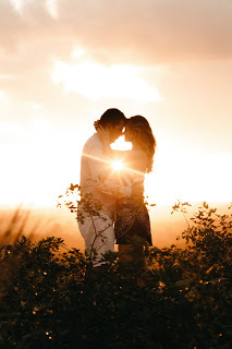 Young couple standing in long grass at sunset with their foreheads touching while hugging each.