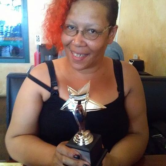 Author Sumiko Saulson (an African American nonbinary person with orange hair) holding a star shaped Mixy Award in hir hands
