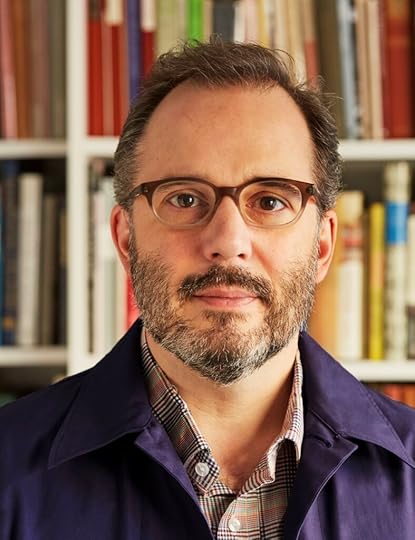 russell maret wearing glasses standing in front of built-in shelves of books
