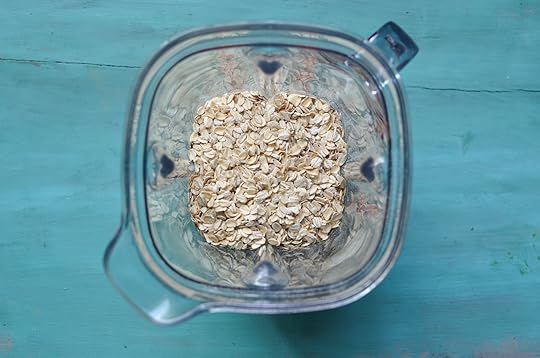 Blender container half filled with rolled oats on a blue background.