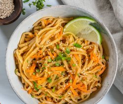 Bowl of Sesame Salad with Two Wedges of Lemon on a Grey Surface