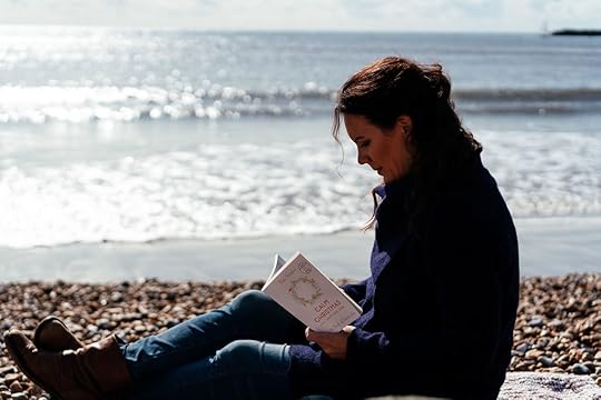author reading Calm Christmas USA book sitting on the beach, sea in the background