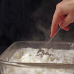 hand holding fork to fluff the baked rice with steam rising.
