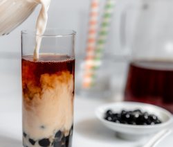 Tall Glass with Boba Tea and a Jug of Plant-Based Creamer Pouring into it