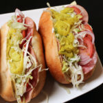 Italian sub sandwiches on platter bursting with cold cuts and other fillings.