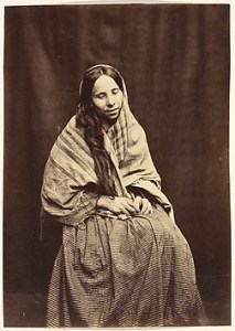 Sepia print photo of a seated woman with scarf and long dress gazes downward.