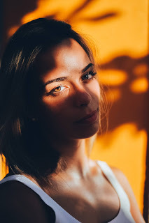 A woman leans against a wall wearing a white singlet with the sunset glowing golden on her eyes.