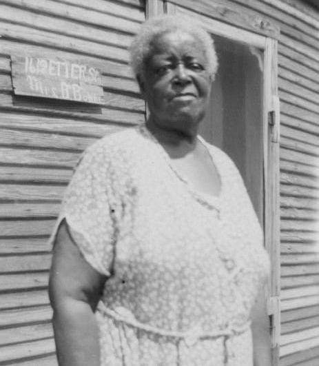 Betty Bormer stands outside a wood-frame house in Fort Worth, wearing a simple dress, looking at the camera., in 1937.