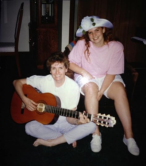 Gaile sitting on the floor holding her guitar with me sitting in a chair wearing in a large white hat with a flower, oversized pink t-shirt, white shorts and white sneakers