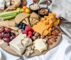 board with various vegan cheese, fruits, and nuts on a brown board with a white background
