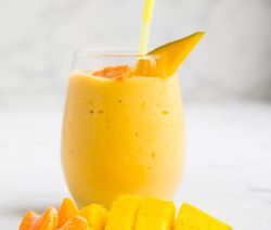 large glass filled with citrus mango smoothie with a yellow straw and some sliced mango and tangerine in the background