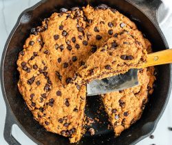 black skillet with chocolate chip cookie and slice cut out with a white background