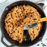 black skillet with chocolate chip cookie and slice cut out with a white background