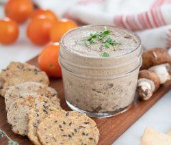 mushroom pâté in a glass container on a brown board with various ingredients in the background