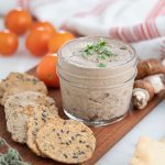 mushroom pâté in a glass container on a brown board with various ingredients in the background
