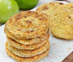 stack of fried green tomatoes on a white background with green whole tomatoes in the background