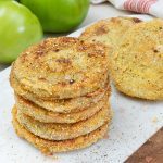 stack of fried green tomatoes on a white background with green whole tomatoes in the background