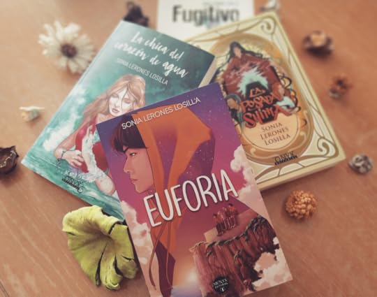 En la imagen aparecen mis cuatro novelas superpuestas: Euforia, La chica del corazón de agua, La posada Shima y Fugitivo adornadas con flores secas alrededor, haciendo un círculo.