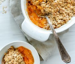 two white bowls of apricot crisp with a metal spoon in one container with a white background