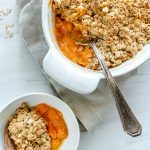 two white bowls of apricot crisp with a metal spoon in one container with a white background