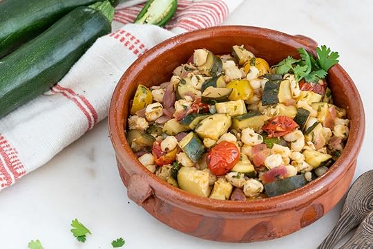 brown bowl with zucchini and hominy with a red and white cloth in a white background