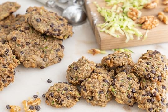 several banana zucchini cookies on a light colored surface with a cutting board and more cookies in the background