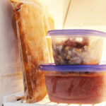 freezer meals in bag and plastic containers stacked on freezer shelf.