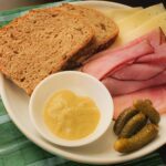 plate of sourdough rye bread slices with ham, cheese, pickles, and mustard.