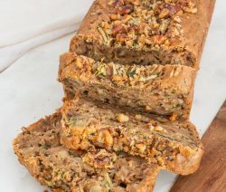 A loaf of zucchini bread sliced on a white cutting board