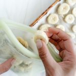 putting sliced bananas into reusable bag with sliced bananas in a white background