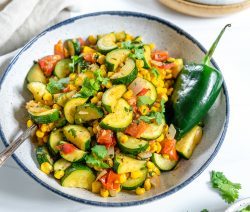 calabasitas recipe with a mixture of veggies in a white bowl with blue rim in a white background