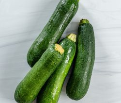 4 zucchinis on a white marble background