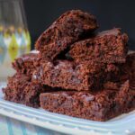 stack of brownies on square plate next to glass of milk and blue and white napkin.