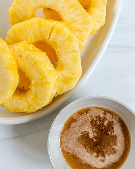 sliced pineapples in a white tray with a small bowl of brown ingredients in a white marble background
