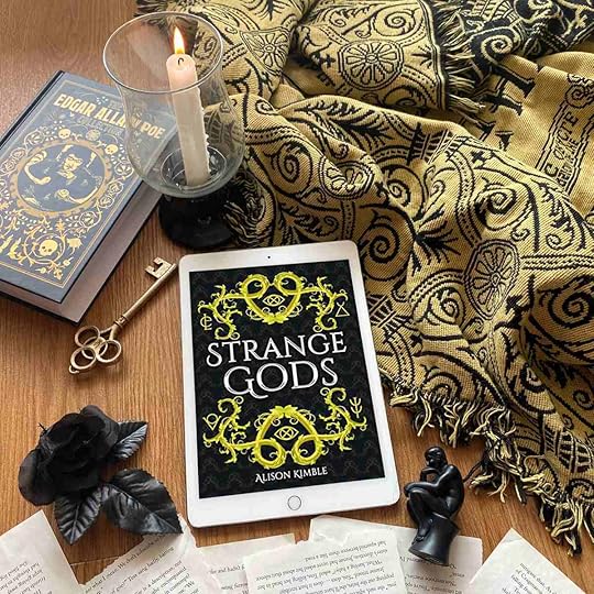 Strange Gods book cover with blanket, book, candle, and black rose