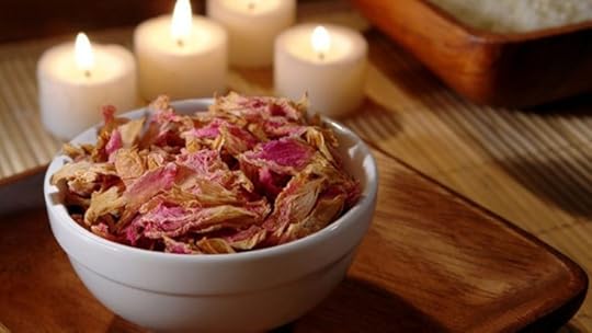 A bowl of potpourri on a table with white lit candles on a wooden table.