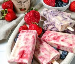 plate of blueberry and strawberry popsicles with ingredients and yogurt in the background