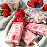 plate of blueberry and strawberry popsicles with ingredients and yogurt in the background