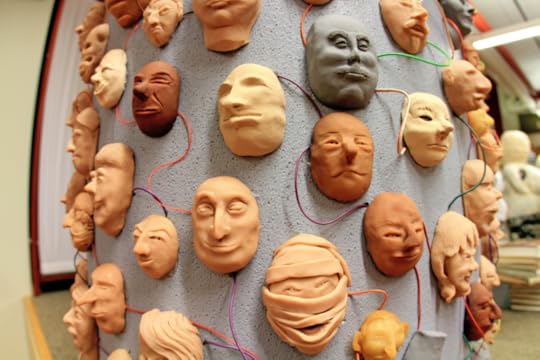 Image: sculpture of many faces attached to a column, all connected to one another by colorful wires.