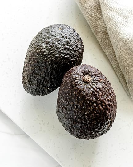 Two Hass avocados on a white surface