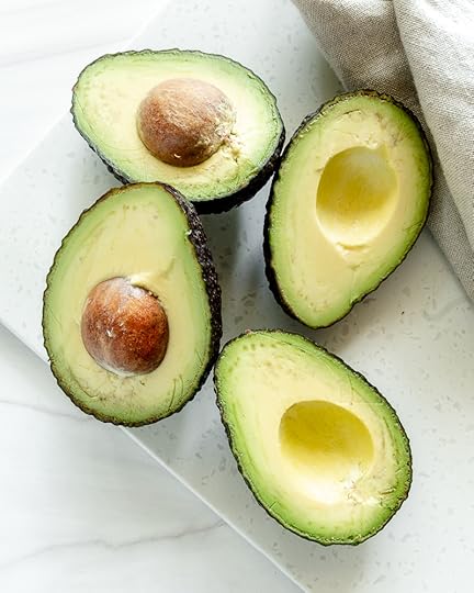 Two halved Hass avocados on a white surface