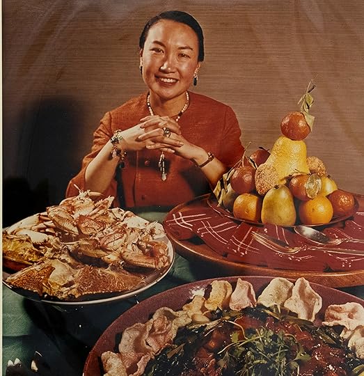 Jade Snow Wong, wearing red dress with hair pulled back, seated behind a table with Chinese food..